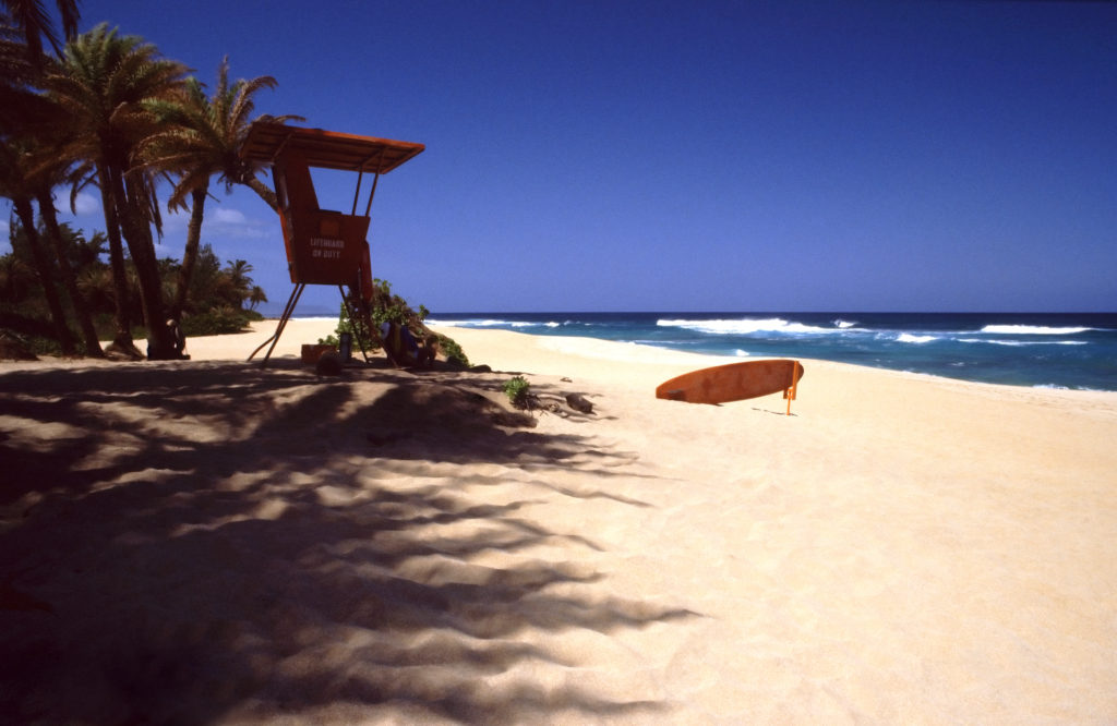 A surfboard sitting on the beach next to an umbrella.